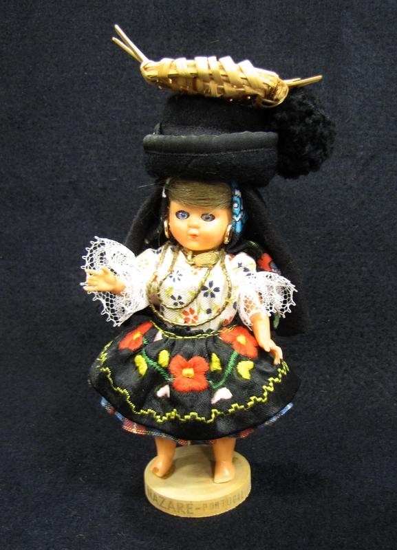 21 736:82.  Docka föreställande flicka med 8 lager av kjolar där den yttersta är svart med blomsterbroderi i rött och gult, vit blus med blommönster, guldsmycken, svart huvudduk samt stor svart hatt med korg överst.Material: Textil, plast, trä. Inköpt: Funchal på Madeira, 1970. H. 15,5 cm.

Dockan ingår i en samling med 106 dockor från olika länder.

Ägarinnan började samla dockor på 1930-talet.Under de kommande åren kom hon allt mer att inrikta samlandet på souvenirdockor som inköptes under resor, framförallt i Frankrike.

Samlandet fortsatte fram till 1980-talet. I hemmet var de flesta dockorna uppställda i monter eller på hyllor.



Under flera år förestod ägarinnan Älvsborgsslöjd i Trollhättan.