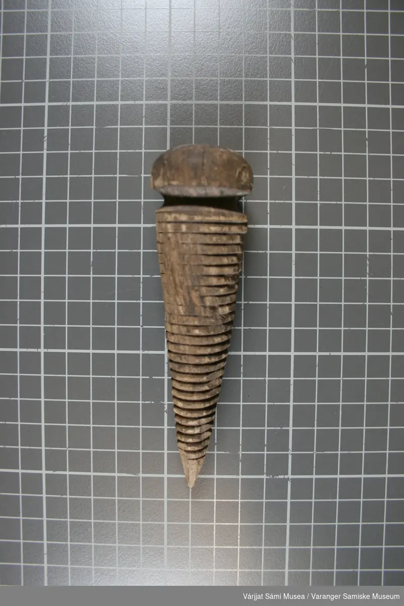 En kjegleformet gjenstand laget av bøk eller eik. Øverste del er dreid i benk, nederste del er spikket grovt og gjengene er laget med maskin.