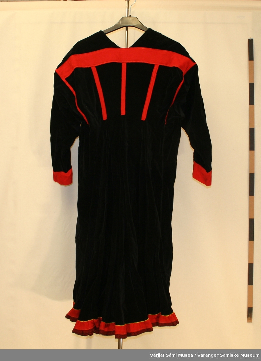 Damekofte av svart fløyel.. Kofta er veldig vid. 3 røde striper på ryggen. Rødt klede på armene. Holbien lik polmakkoften, en jarekant