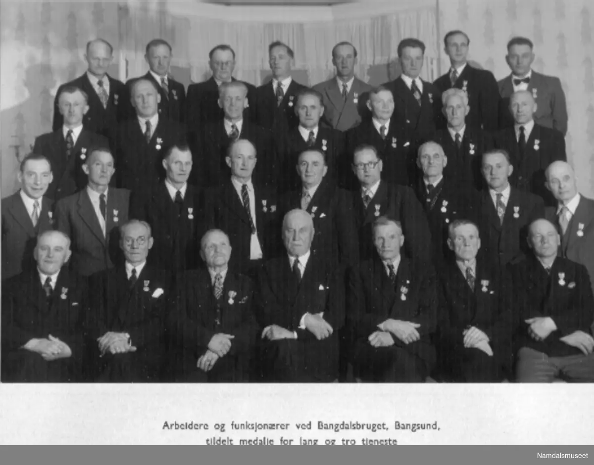 26.06.1954. Arbeidere og funksjonærer ved Bangdalsbruket, tildelt medalje for lang og tro tjeneste, 25. juni 1954. Navnene står bakpå pappen.