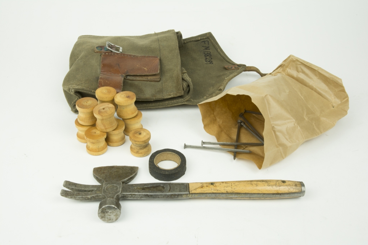 Verktygsväska av tyg med hakar för fastsättning i bälte. Väskan innehåller träknoppar, eltape mm. På väskan hänger en hammare