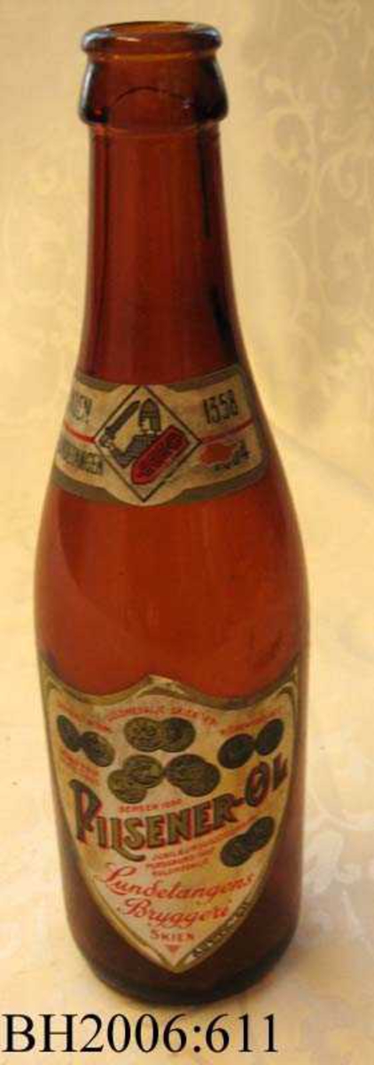 Ølflaske av brunt glass med  etikett av papir på flaskens front. 