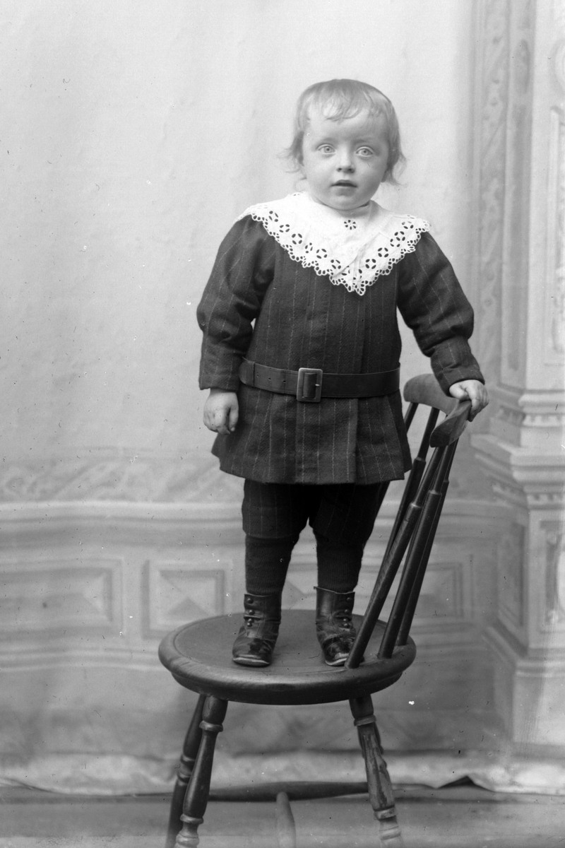 Studioportrett i helfigur av et barn stående på en stol.