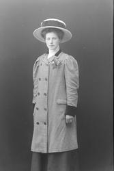 Studioportrett av en kvinne med hatt og rutet kåpe.