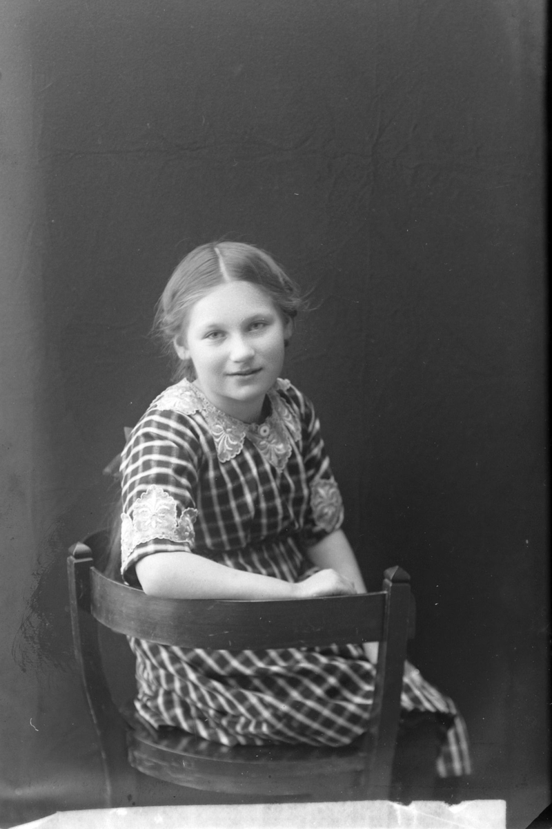 Studioportrett av en ung jente i en rutet kjole.