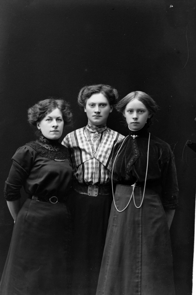 Studioportrett av tre kvinner foran en mørk bakgrunn.