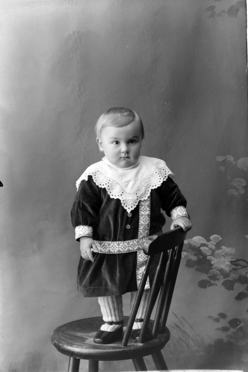 Studioportrett av et lite barn som står på en stol.