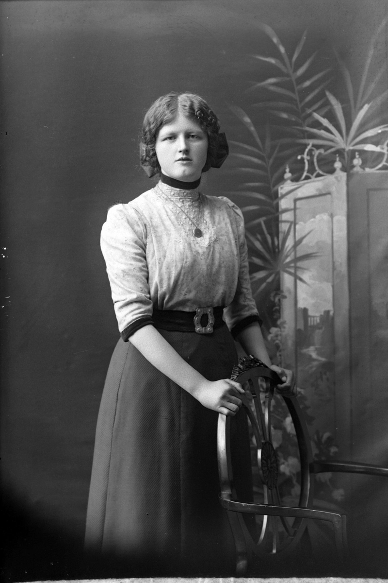 Studioportrett av en kvinne med hendene på en stolrygg.