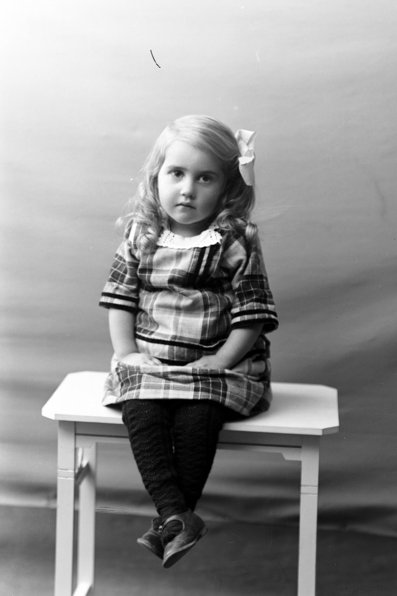 Studioportrett av en liten jente på et bord.