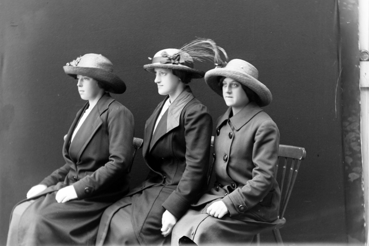 Studioportrett av tre sittende kvinner sett i profil.