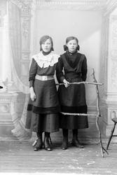 Studioportrett av to kvinner med et gjerde foran seg.