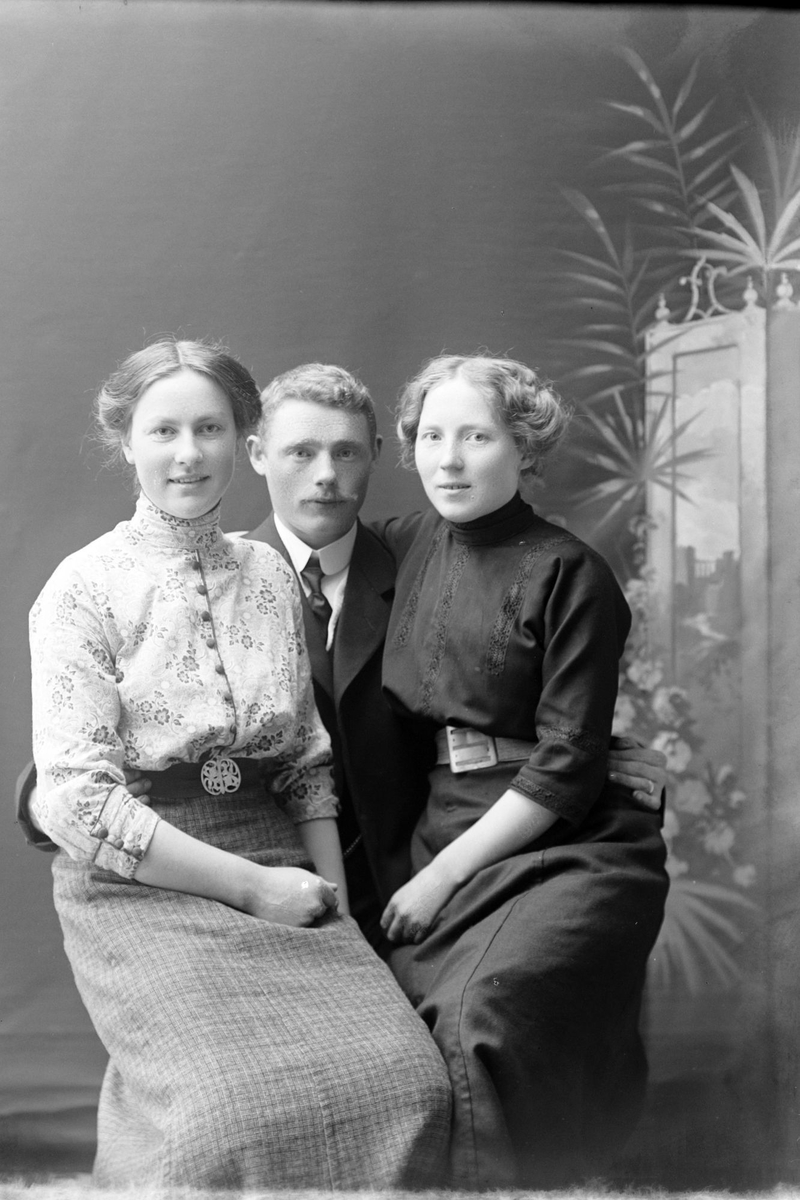 Studioportrett av to kvinner som sitter på en manns fang.