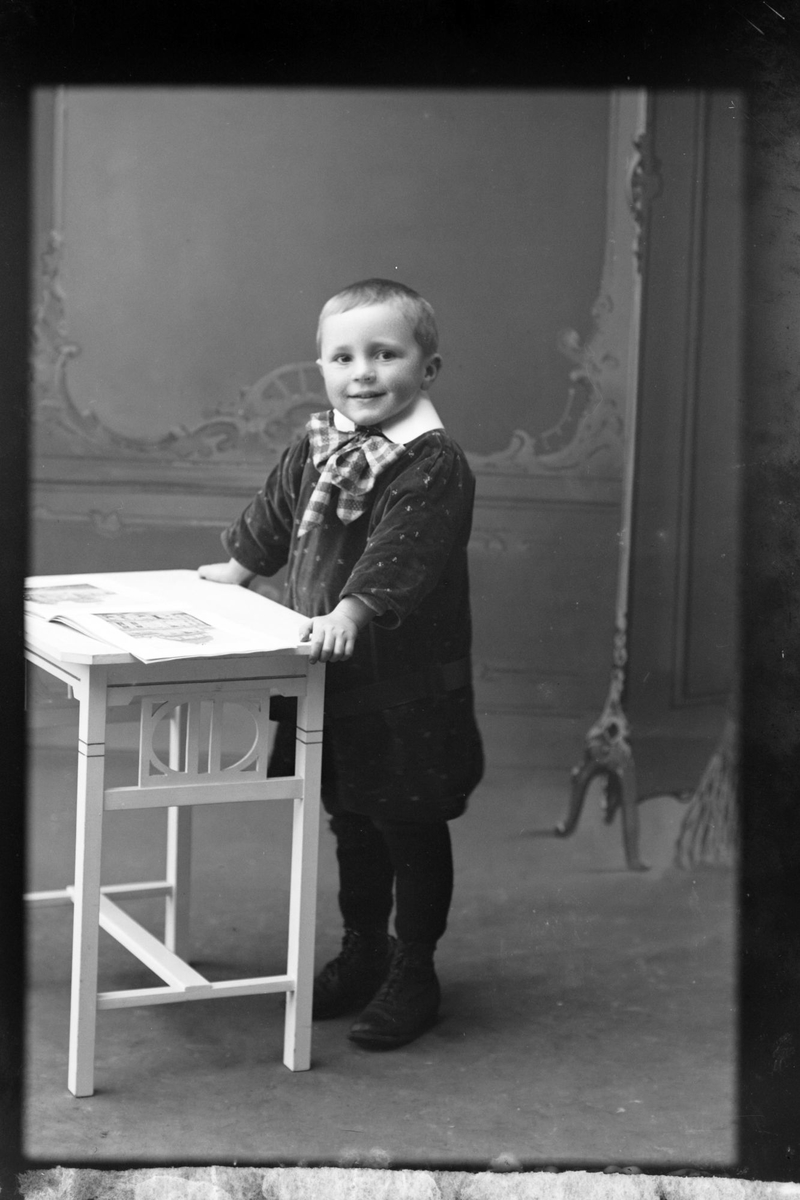 Studioportrett av en liten gutt i helfigur, muligens Evald Olsen.