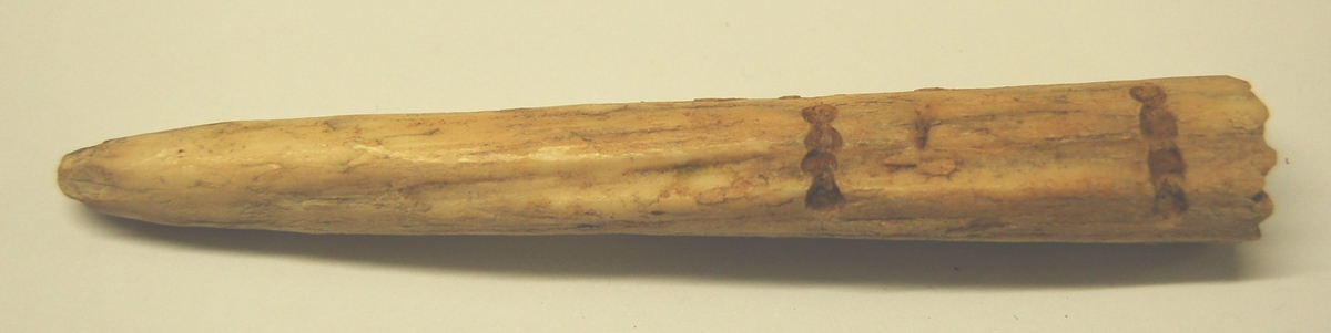 Gjenstanden er laget av spissen på et narrkvalspyd. 1,5 og 5,0 cm. inn fra tverenden, er det "fræst" ut 2 groper, henholdsvis 1,5 og 1,7 cm. lange, på tvers av spydet.