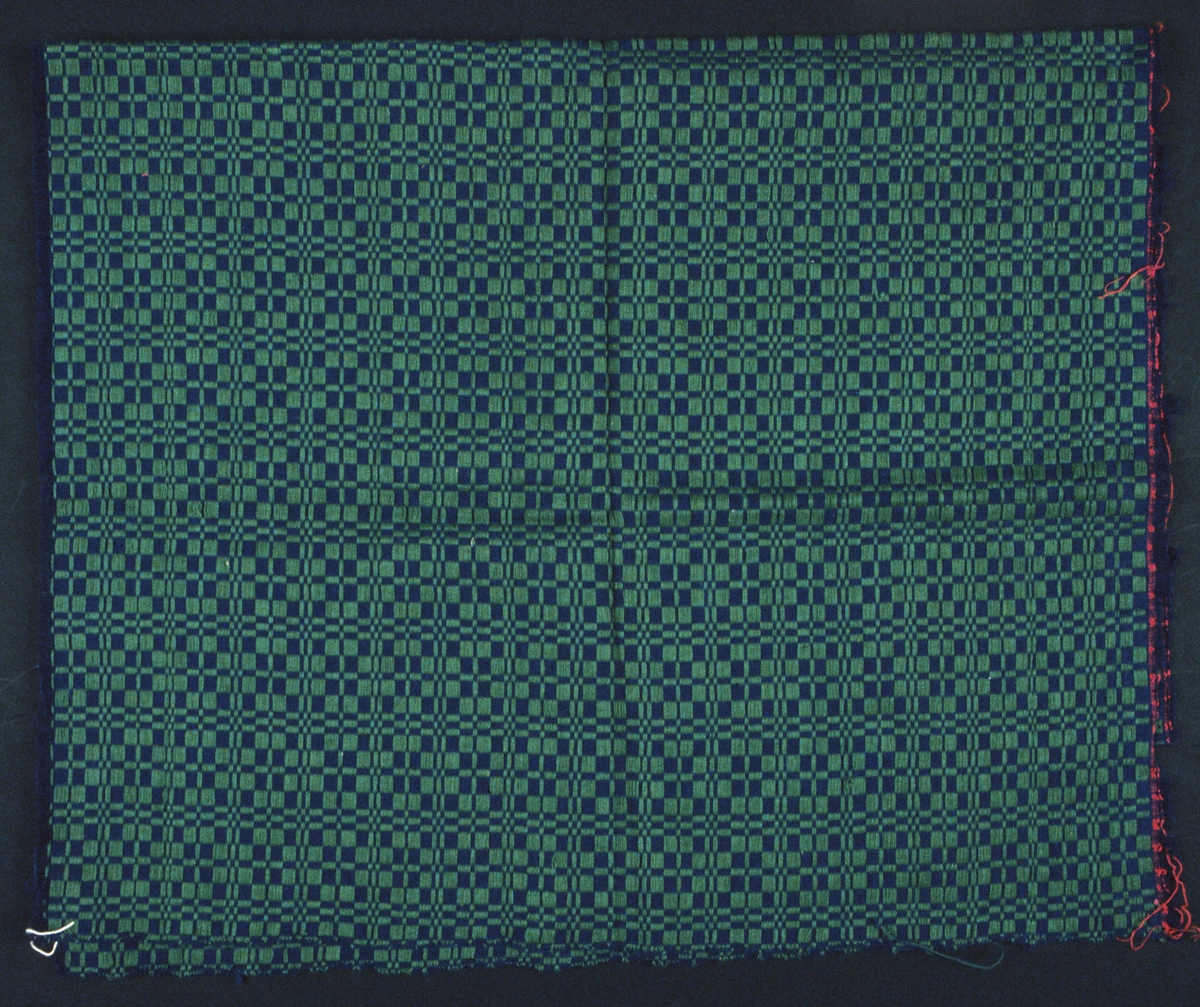 Vävprov i munkabälte. Olika nyanser blått, nära liggande varandra, i varp och inslag. Grönt yttäckande mönster. En 80 x 90 mm stor ruta i ena hörnet är bortklipp. Stadkant i två sidor, varpen är avklippt i båda ändar.
Varp i blått 2-trådigt s-tvinnat bomullsgarn, 18 trådar/cm.Botteninslag i blått 2-trådigt s-tvinnat bomullsgarn, 30 trådar/cm och mönsterinslag i grönt, 2 trådar tillsammans.
