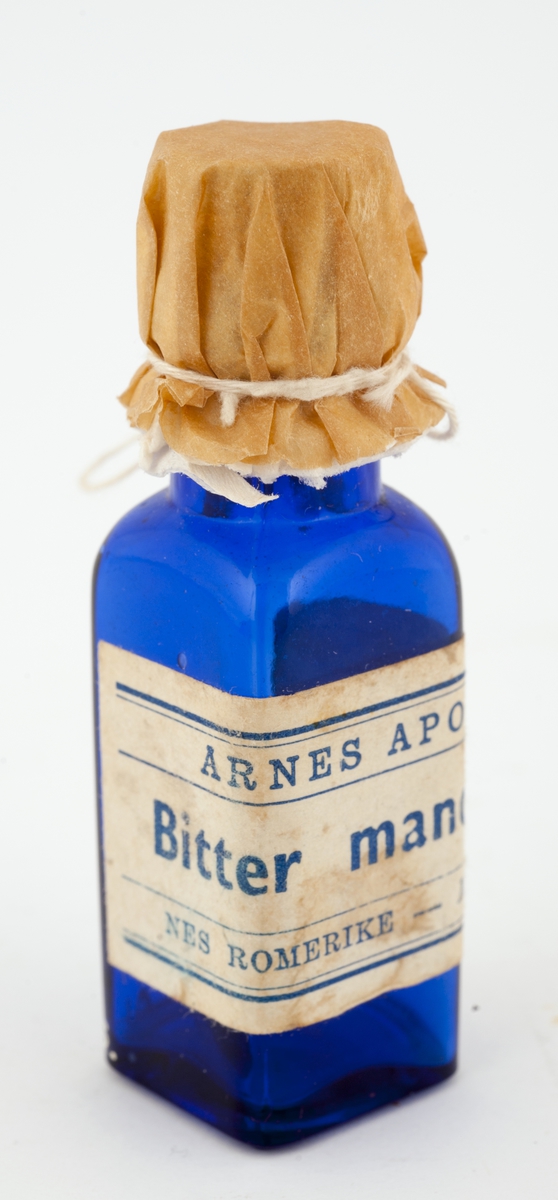 4-kantet flaske med kork og tektur med hyssing.
Hvit etikett med  blå dekor og skrift.