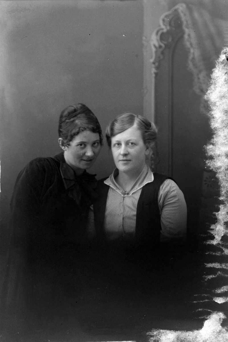 Studioportrett av to kvinner i halvfigur. Bildet er delvis ødelagt.