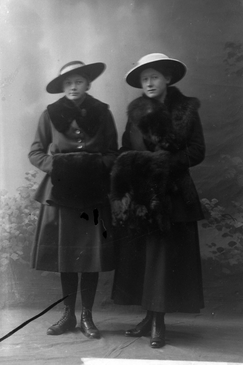 Studioportrett av to kvinner med pelsmuffer.