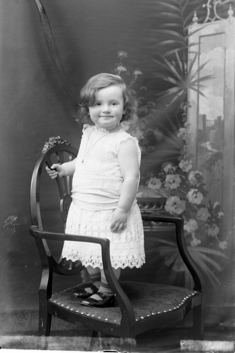 Studioportrett av en liten jente som står på en stol.
