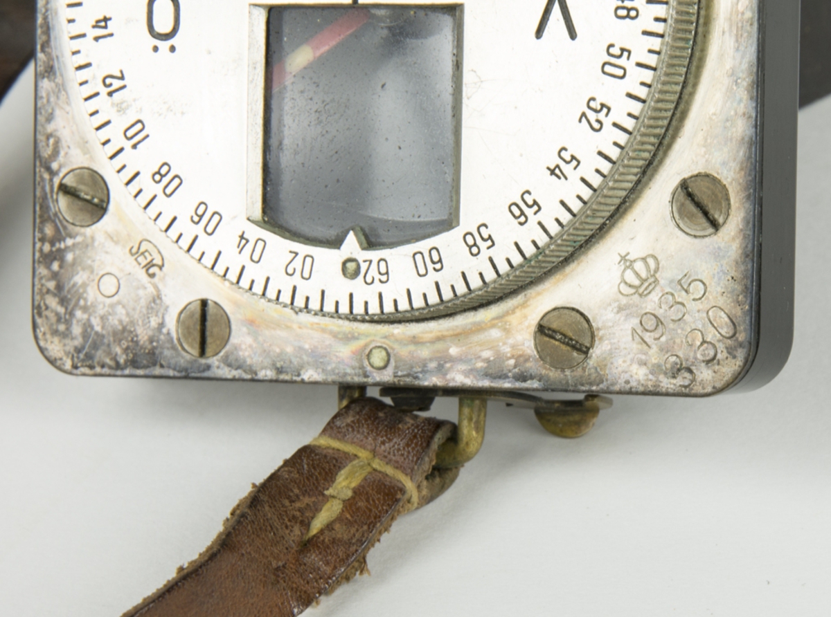 Kompass med hopfällbart lock i bakelit. Kompassen är fäst i en läderrem.
