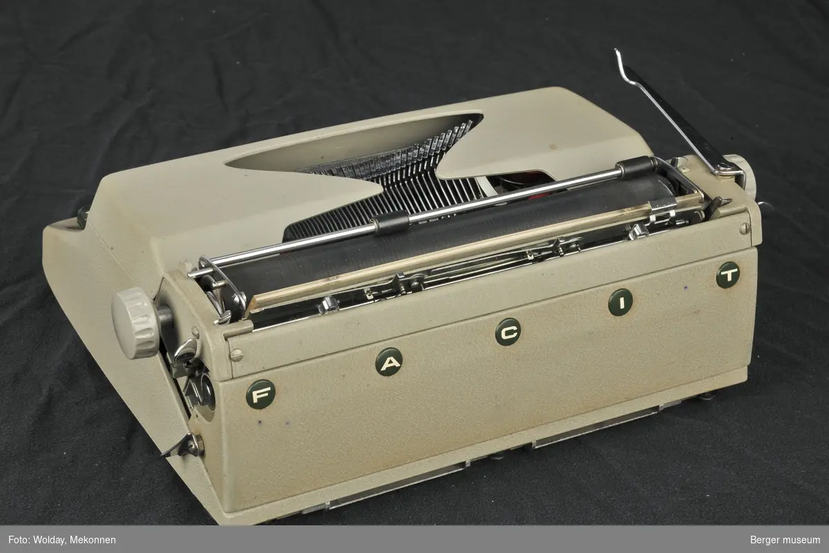 Reisekoffert med skrivemaskin. Skrivemaskinen er festet til koffertens nedre del, men den kan tas av. Kofferten er todelt med lokk. Kofferten kan låses og det medfølger nøkkel. Innunder lokket er det en lomme til papirer.