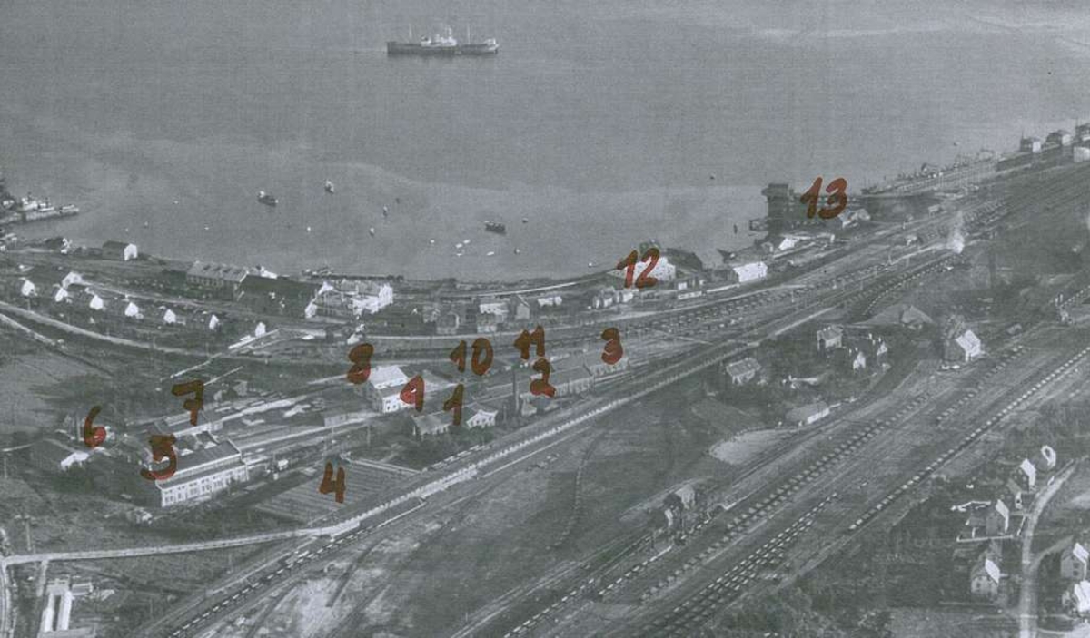 Kirkegata nederst til h. med forgrening til Stormyrveien og Malmveien. Øvre rangerstasjon med Lokstall 2 i bakkant. Noen av husene mellom Øvre Rangerstasjon og Nedre Rangerstasjon ble senere flyttet over til Malmveien.  Fagerneslinja helt til venstre i bildet. Nedrelinja går henimot diagonalt  til Nedre rangerstasjon. I mellom de to jernbanesporene i nedre venstre hjørne ses Narvik Handelsgartneri som startet virksomheten sin ca. 1934. Forbindelsessporet fra nedre rangerstasjon til brua ved Sjøbakken dannet et triangel med Fagerneslinja og nedrelinja. Når lok og skinnegående materiell kjørte "Triangelen" ble materiellet snudd i lengderetningen. NSB`s verkstedtomt med mekanisk verksted og lokverksted i venstre ende. Bak lokverkstedet ses det nye snekkerverkstedet.  Til høire for det lager, forådsbygg med kontor samt tre lokstaller.. LKABs verksteder og provisorisk malmkai.  Helt til v. slepebåtene og bak dem kullkaia.  Ankenes i bakgrunnen.