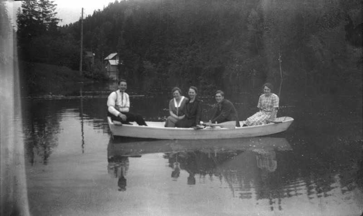 Fem personer i en robåt på et vann.