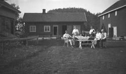 Gruppe ved dekket bord på et gårdstun. Aagot Olausssen med h