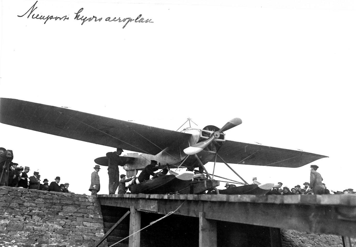 Ett fly på ei kai, Nieuport. Flere personer ved flyet.