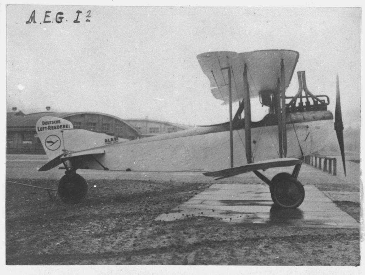 Ett fly på bakken. A.E.G. C I. Hangarer i bakgrunn