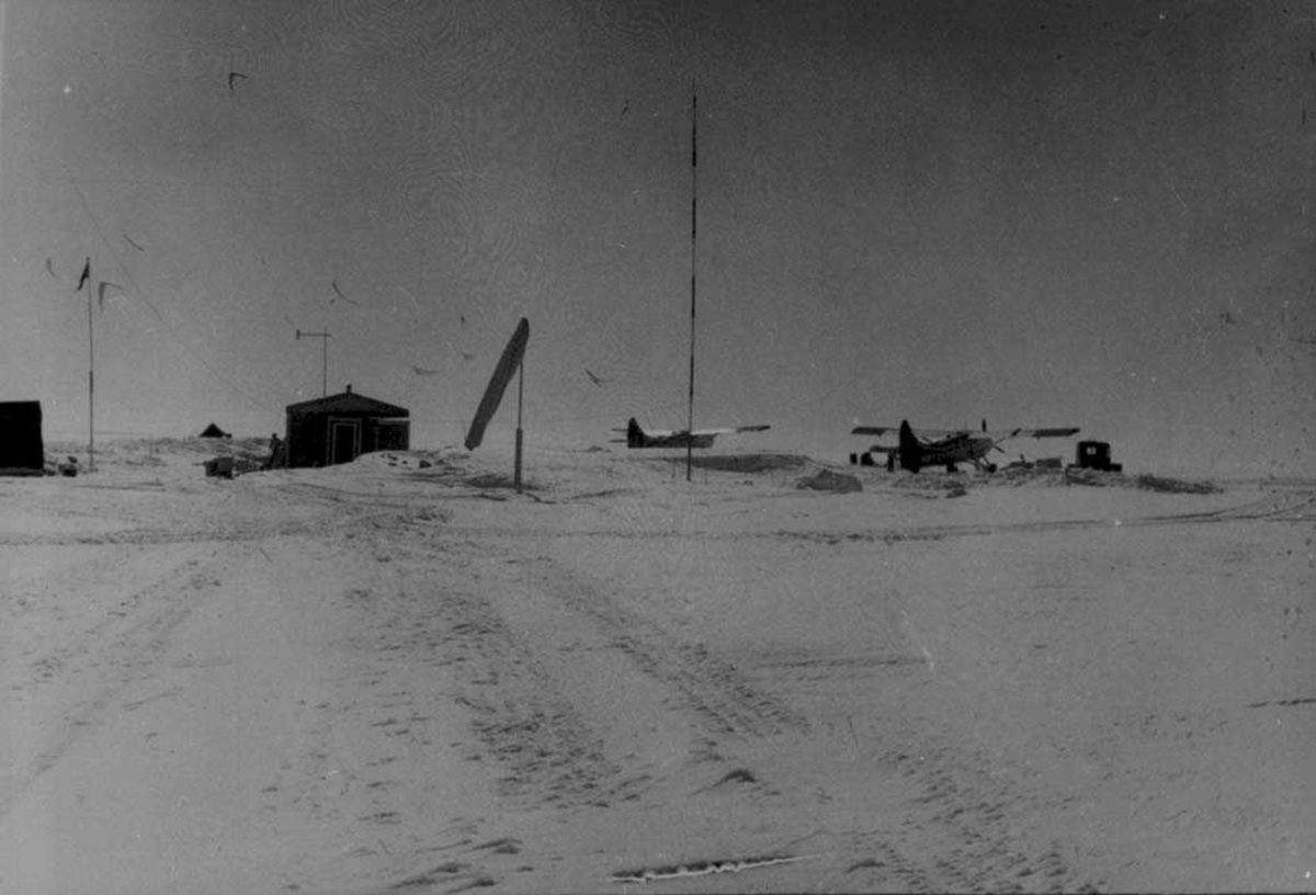 To fly på isen, Otter OAG og OAF. Små bygninger, radiomast og annet utstyr ved flyene.