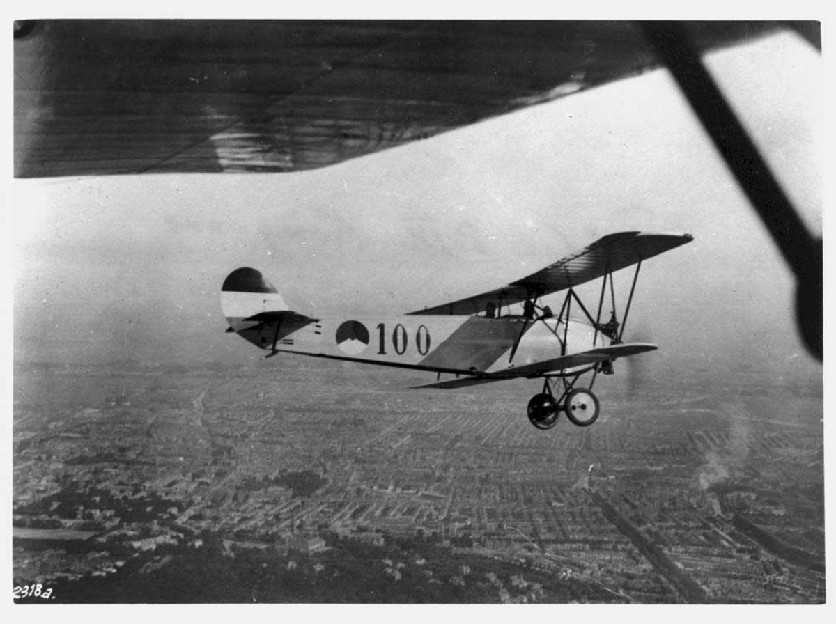 Luftfoto. Ett fly i lufta, Fokker S.IV, 100. Tettsted med havneområde under.