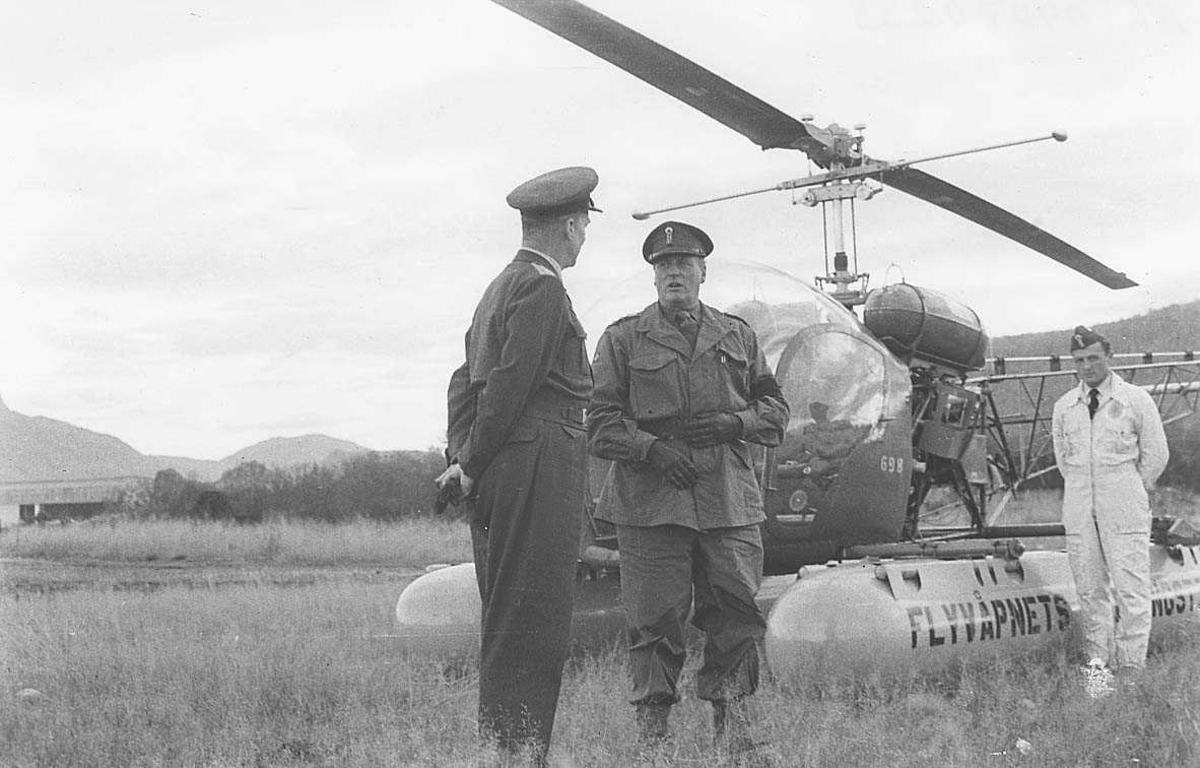 2 offiserer i samtale Kong Olav og Odd Bull 1 person i bakgrunnen ved siden av et helikopter.