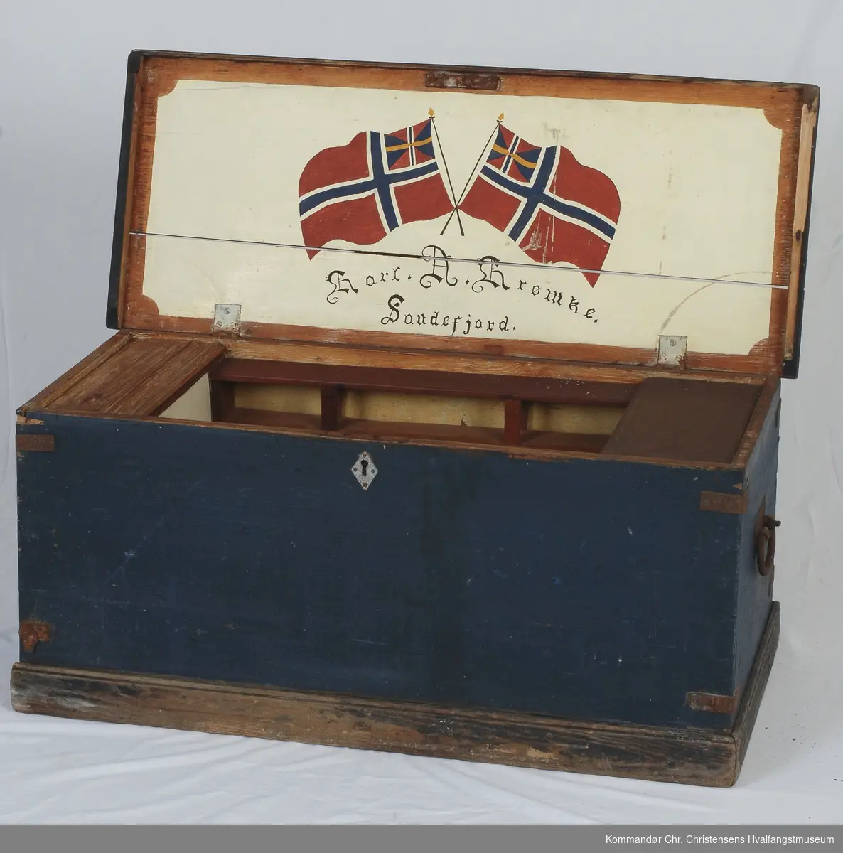 Flatt, hengslet lokk. Invendig leddik på hver kortside, hylle langs ene langside. Dekor innside av lokk: To norske flagg med unionsmerke. 