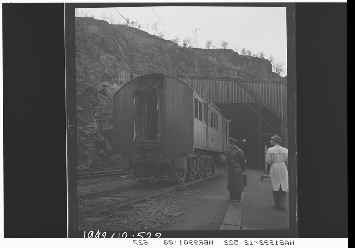Del av et lokomotiv foran Kapp Horn tunnelen ved Katterat.  To menn stående utenfor. Mannen til venstre er passkontrollør Ellingsen.
