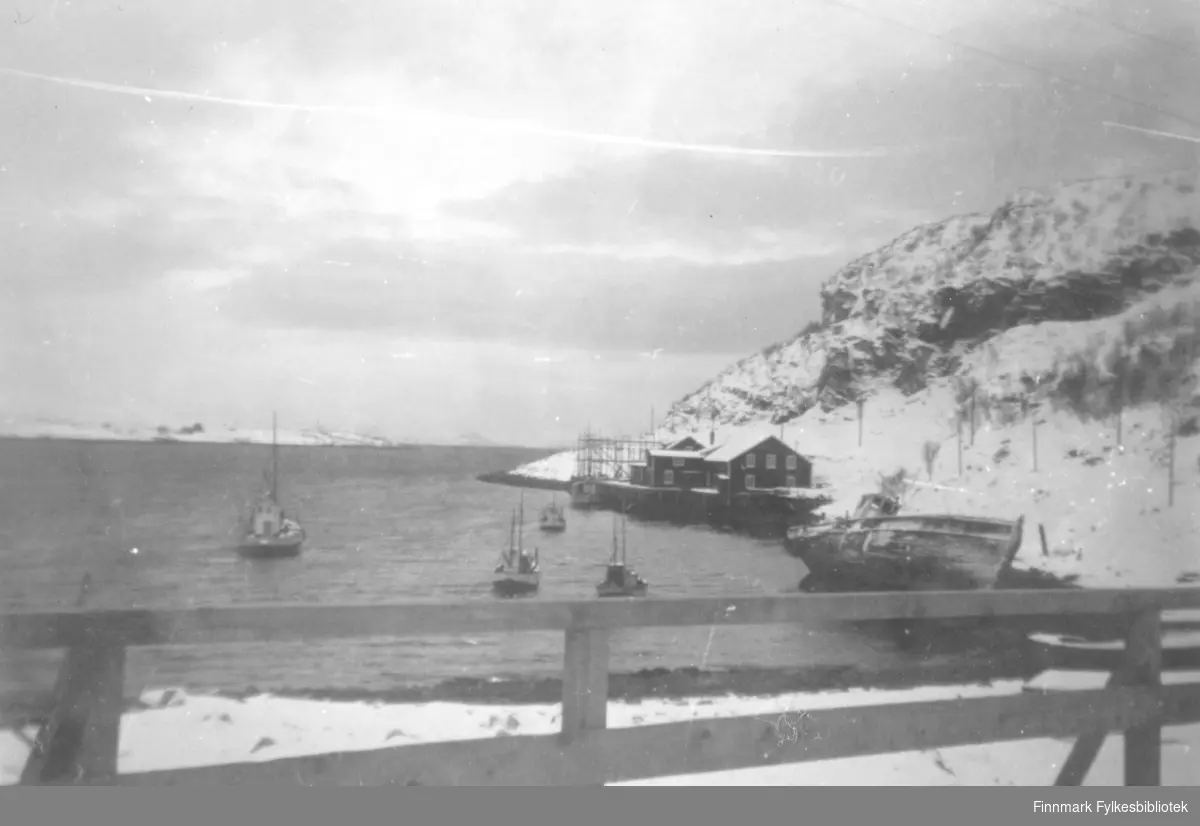 Evald Valens fiskebruk i Lillefjord (Litlefjord). Det ligger flere båter ute på vannet. Båten til venstre var Evalds livbåt. På kaia står det nothjeller. Snøen ligger på bakken
