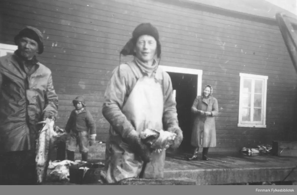 På kaia i Lillefjord (Evald ? Valens fiskebruk). Fra venstre står Jon Amundsen, en ukjent gutt, Abraham Nilsen, og en kvinne ved navn Sara. Mennene holder fisk i hendene