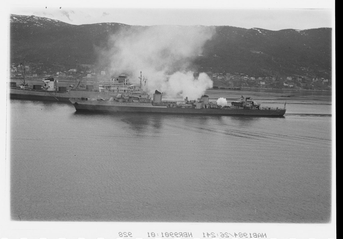 Fransk jager Le Terrible ankommer Narvik havn og utveksler salutt med norske marinefartøy. Markering av 6-årsdagen for gjenerobringen av Narvik. Malmbåt i bakgrunn.