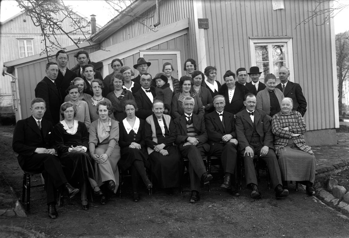Selma (i mitten av främre raden) firar sin 60-årsdag i början av mars 1934 och firas av släkt och vänner. Bilden är tagen utanför huset på Åsenvägen 71 i Mariebo 10, Jönköping. På en skylt på husgaveln står "Kv Odygden nr 3". 