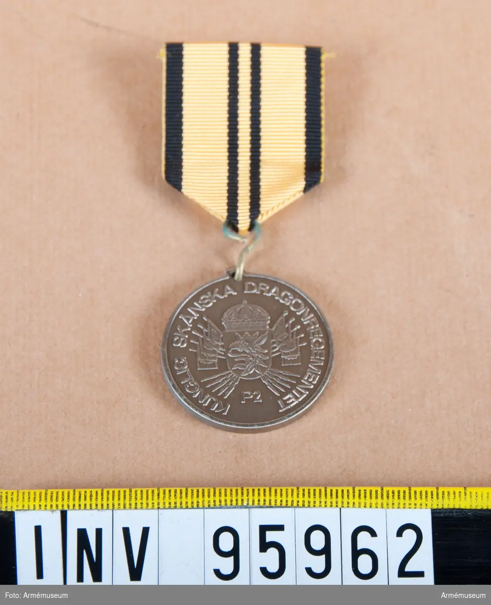 Skånska dragonregementets (P 2) minnesmedalj 1 i silver, 8:e storleken.

Band: gult med svarta kanter och två svarta ränder på mitten.