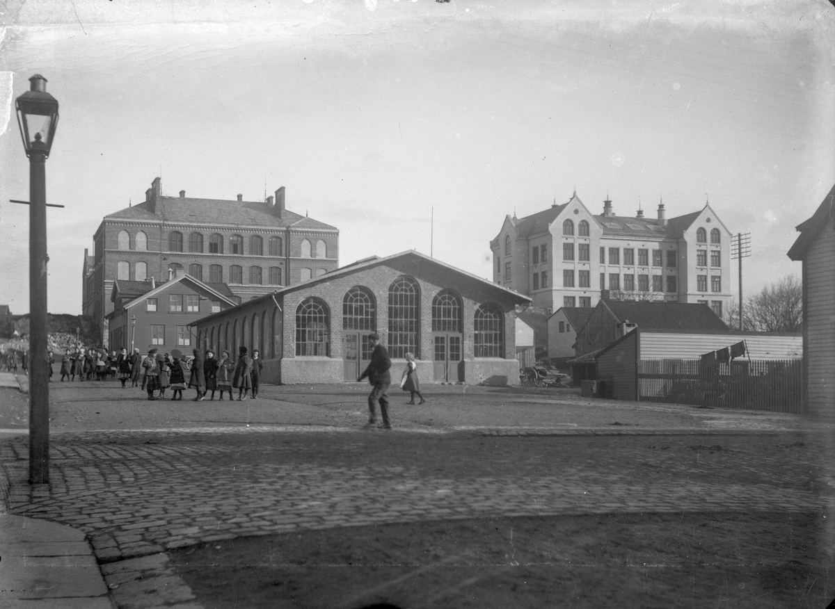 Torvbakken og Breidablikk (skole). Gatelykt til venstre. Noen personer midt på bildet. Flere til venstre i bakgrunnen. Tregjerde til høyre.