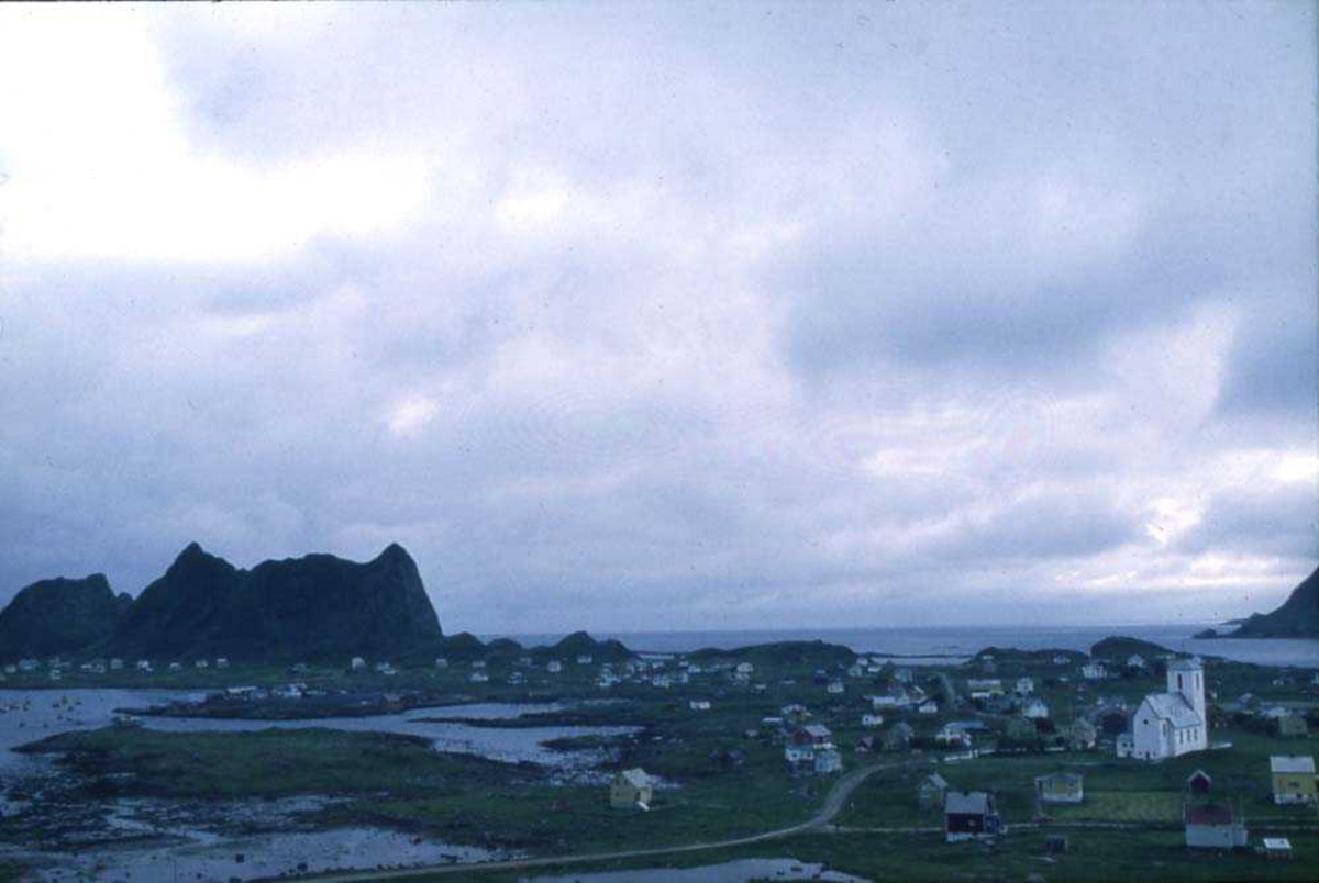 Landskap. Værøy i Lofoten. Parti fra tettstedet med kirka dominerende i bildet. Videre ses Sørland med karakteristiske fjell i bakgrunnen.