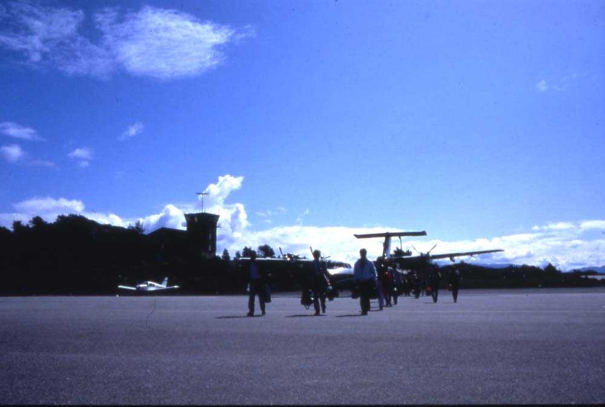 Lufthavn/flyplass. Florø. Et fly, DHC-7-102 Dash7 fra Widerøe har nettopp landet. Passasjerer forlater flyet på vei til ekspedisjonen.
I bakgrunn Flytårnet.