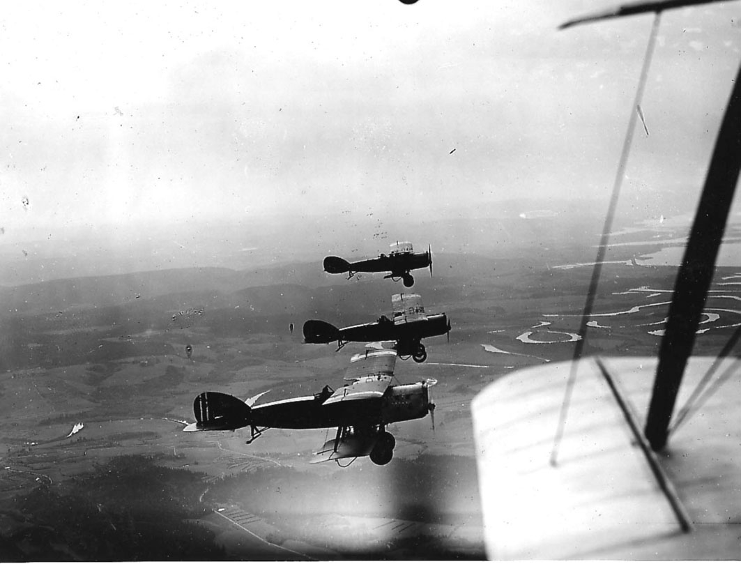 Luftfoto, tre fly i luften, Bristol Fighter. Landskap under. Litt av vinge og stag på ett fly, hvor bilde er tatt fra, i forgrunnen.