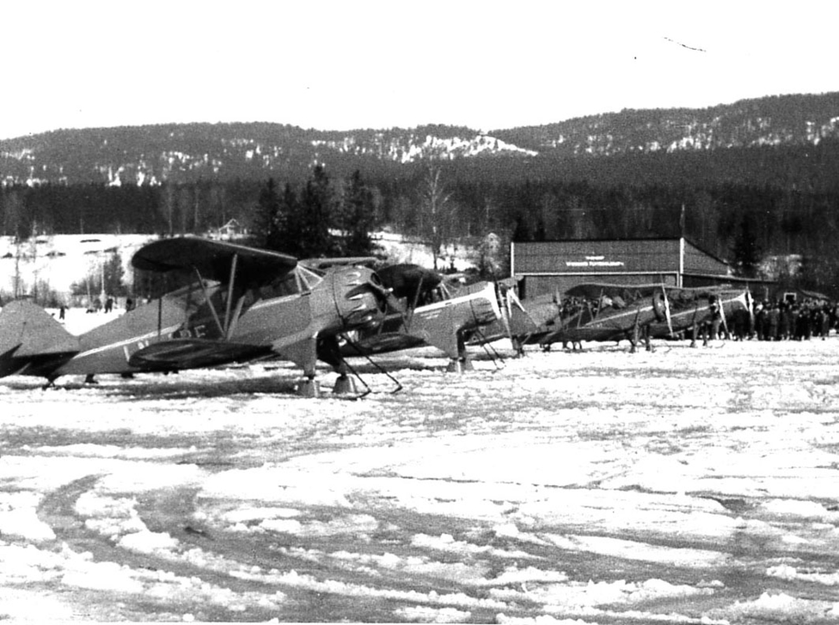 Åpen plass, flere fly med skiunderstell, fra Widerøe. Snø på bakken.