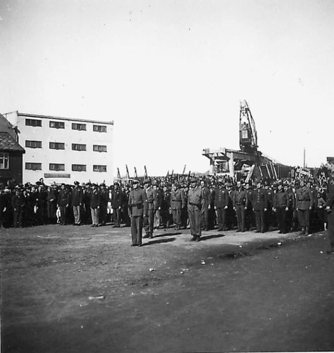 Frigjøringsdagene i Bodø etter krigen  1945. Mange personer oppstilt nede ved kaiområdet. Sivile og militære. Kullkranen til Jakhelln i bakgrunnen.