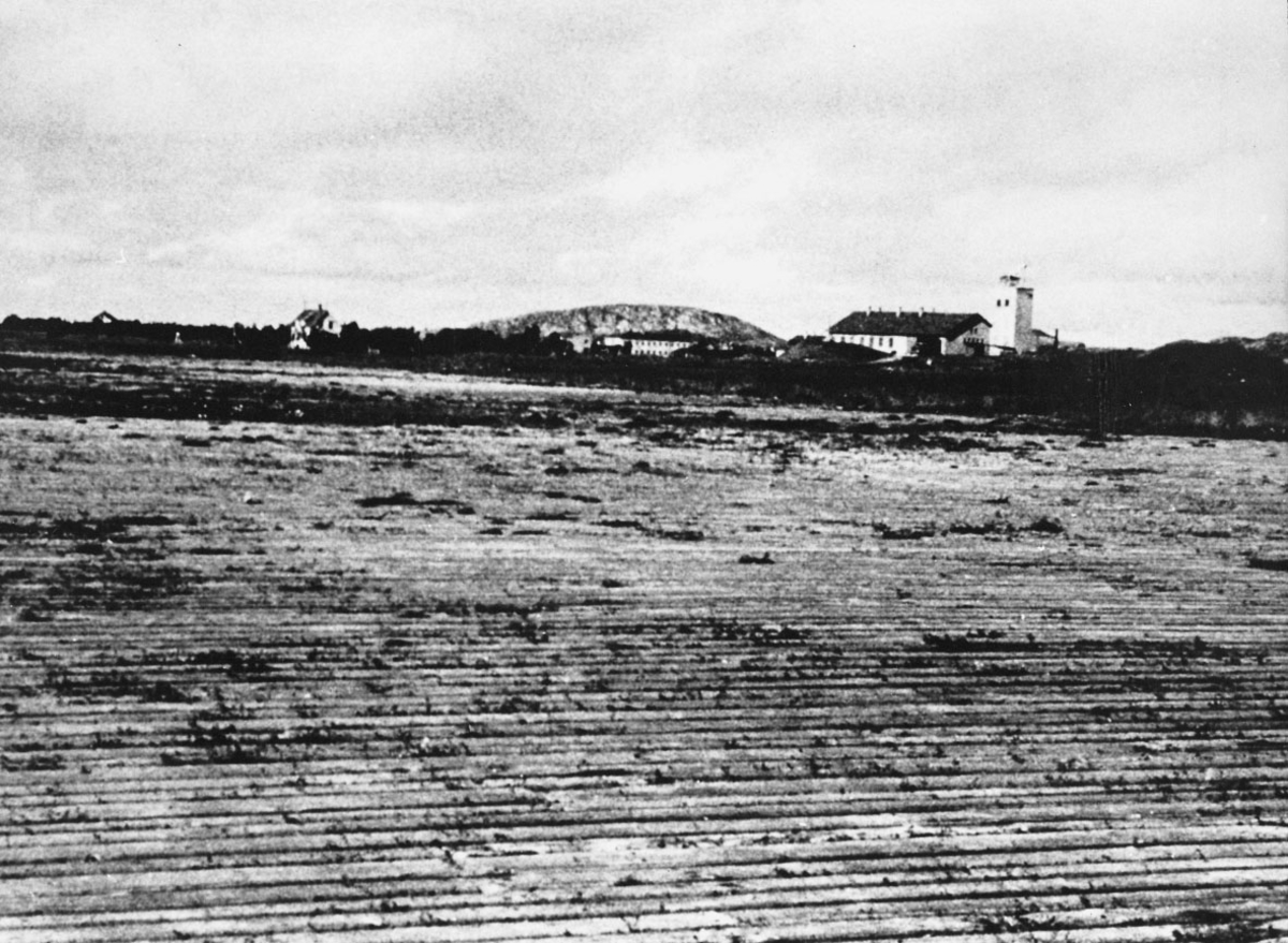 Bodøs første flyplass, "plankeflyplassen". Noen bygninger i bakgrunnen, bl.a. brannstasjonen til høyre.