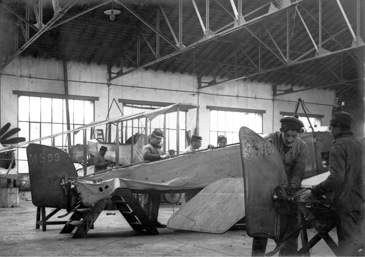 Fra flyverksted, flyfabrikk. Fly, Morane-Saulnier, under bygging. Flere personer i arbeid.