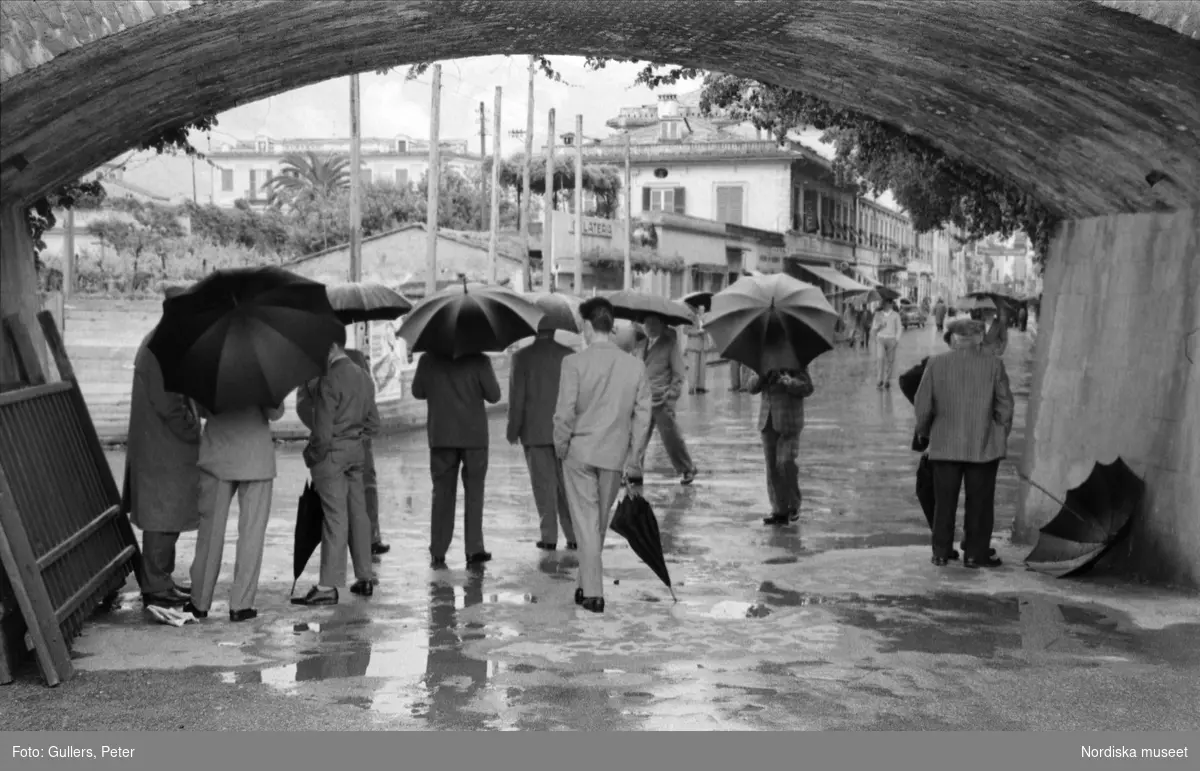 Män med uppfällda paraplyer under ett brovalv.