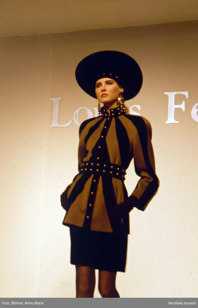 Modevisning. Modell i randig jacka i brunt och svart, svart kjol och hatt. Från Louis Féraud.